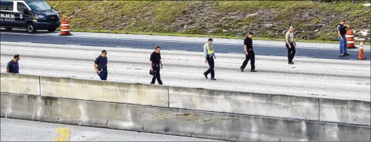  ??  ?? Police scour the roadway for evidence as they investigat­e the area where the car was found with the shooting victim inside. He was transporte­d to a hospital and declared dead.