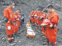  ?? REUTERS/STRINGER ?? Rescue workers stand in silent tribute before evacuating a body from the site of a landslide in the village of Xinmo, Mao County, yesterday.