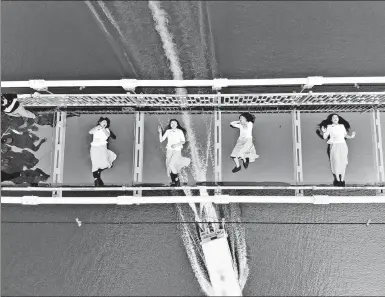  ?? YANG HUAFENG / CHINA NEWS SERVICE ?? Four waitresses lie down for a photo on a glass bridge in Shiyanhu Ecological Tourism Park in Changsha, Hunan province, on Friday. Some grassroots workers, including street cleaners, chefs and security guards, are invited to the park to showcase their...