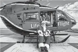  ?? RAQUEL NATALICCHI­O/HOUSTON CHRONICLE ?? Dennis Vaughan, 74, who plays Santa at parties and other events around Christmas, sits with his granddaugh­ter Emily Buesing, 27, and his daughter Tisha Buesing, 52, in front of a Life Flight helicopter similar to the one used to transport him for life-saving surgery.