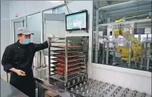  ??  ?? A canteen staff member puts dishes cooked by the robot on a conveyor belt.