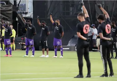  ?? AP Photo/John Raoux ?? ■ Orlando City players, left, raise their fists in the air in solidarity with other MLS teams before the start of an MLS soccer match Wednesday in Kissimmee, Fla., while wearing shirts and masks with messages about race.