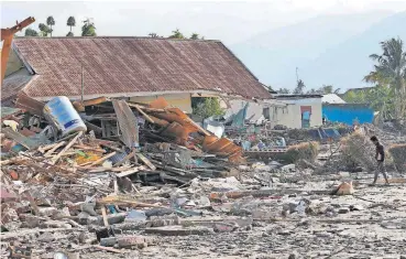  ?? [AP PHOTO] ?? A man walks by houses damaged Monday following a massive earthquake and tsunami at Talise beach in Palu, Central Sulawesi, Indonesia.