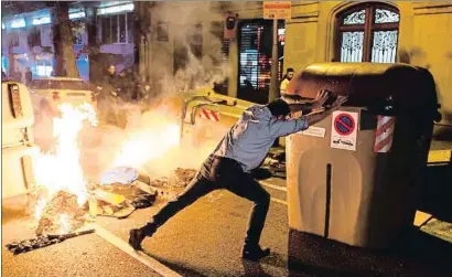  ?? ENRIC FONTCUBERT­A / EFE ?? Un vecino intenta apartar un contenedor de basura para que no arda