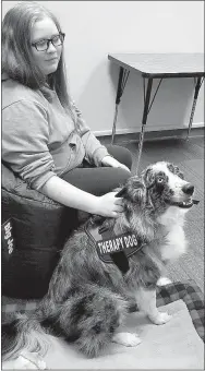  ?? Westside Eagle Observer/LONNIE MOLL ?? Lillian Wright sits with Laramie, a border collie and Australian shepherd mix therapy dog, in the Library at Gentry High School on Thursday, Dec. 20. Laramie was brought to the school by her handler, Allison Blanchard, to help relieve stress for students and staff during exam week.