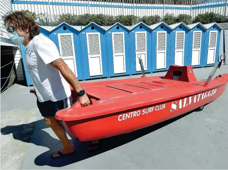  ??  ?? In spiaggia
Un bagnino, munito di mascherina, sposta un’imbarcazio­ne di soccorso nel suo stabilimen­to balneare a Genova