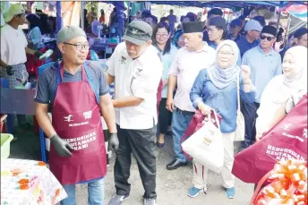  ?? ?? Len Talif puts an apron on one of the traders at the Sarikei Ramadan Bazaar.