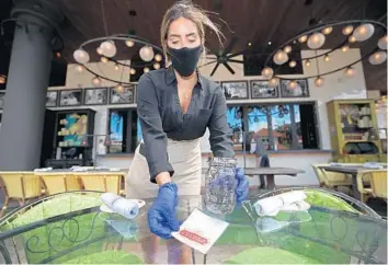  ?? JOHN MCCALL/SOUTH FLORIDA SUN SENTINEL ?? Server Nadia Rose puts down a card indicating that the table has been cleaned at Louie Bossi’s Ristorante Bar Pizzeria before the Boca Raton restaurant reopened Monday in accordance with Palm Beach County’s phase 1 reopening.