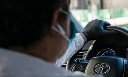  ??  ?? A rideshare driver wears a mask and gloves while driving. Drivers in California are calling for more benefits. Photograph: Jeenah Moon/ Reuters