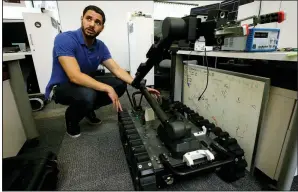  ?? AP/STEVEN SENNE ?? Software engineer Nicholas Otero talks with a colleague at Endeavor Robotics in Chelmsford, Mass., about the features on a reconnaiss­ance and bomb-disabling robot nicknamed the Centaur. The robot is being developed under a $100 million contract.