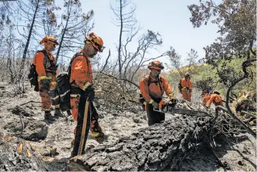  ??  ?? Inmates from the Delta Conservati­on Camp walk back to their engine after looking for hot spots at the Canyon Fire in Napa. Inmates, who account for as much as 40 percent of the men and women who battle wildland blazes, fight fires without water by...