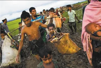  ?? Bernat Armangue / Associated Press ?? Members of the Rohingya ethnic minority from Myanmar carry their children and belongings through rice fields after crossing over to the Bangladesh side of the border near Cox’s Bazar.