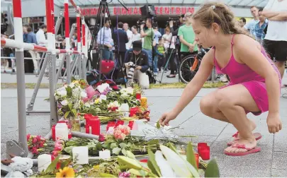  ?? AP PHOTOS ?? MOURNING: A girl, above, puts down flowers in front of the Olympia mall where a lone gunman killed nine people Friday in Munich, Germany. People mourn, below, at the site of the massacre.