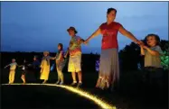  ?? SETH WENIG - ASSOCIATED PRESS ?? People hold hands in a circle around a large, illuminate­d peace sign on the original site of the 1969Woodst­ock Music and Arts Fair in Bethel, N.Y., on Thursday.