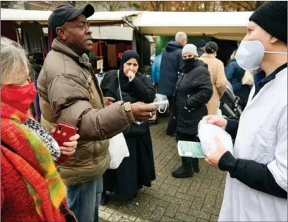  ?? PIERRE CROM / GETTY IMAGES ?? A doctor distribute­s masks in a market in Rotterdam on Nov 27. The Omicron variant had been present in the Netherland­s even before South Africa first reported its detection.