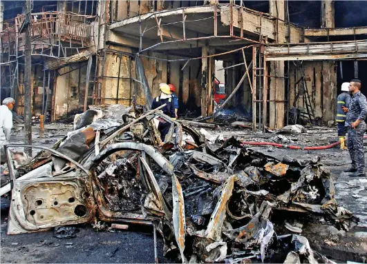  ??  ?? Devastatio­n: The mangled wreckage of the IS truck bomb smoulders outside the Baghdad shopping mall it destroyed yesterday