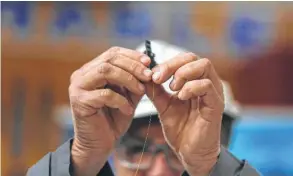  ??  ?? A worker holds a glass strand that will be woven into a fiber optic cable at the SubCom factory in Newington, N.H.