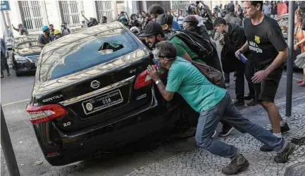  ?? Ricardo Borges/Folhapress ?? Manifestan­tes tentam virar carro em frente à Assembleia do Rio, após aumento da contribuiç­ão de servidores