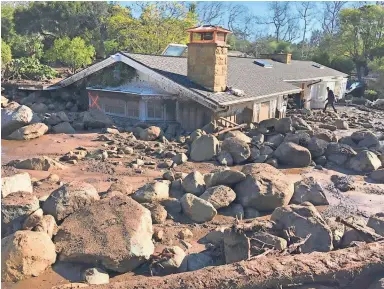  ??  ?? Kerry Mann walks past boulders at the home of a friend in Montecito, Calif., Wednesday, a day after rains caused deadly mudslides. As of Wednesday night, the death toll from the natural disaster had reached 17 and rescuers were looking for at least a...