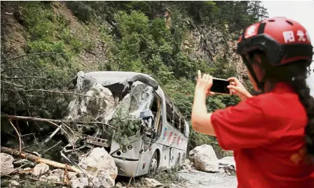  ?? — Reuters ?? For documentat­ion purposes: A rescue worker taking pictures of a bus that was damaged during a rockslide which was triggered by an earthquake outside Jiuzhaigou county.