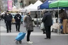  ?? Mary Altaffe/Associated Press ?? A shopper stands on a social distancing marking as police officers patrol the farmers market Wednesday in Union Square in New York.