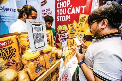  ?? ?? CASHLESS ECONOMY — A consumer pays for the potato chips he bought through cashless e-wallet at a booth in the Cashless Expo 2023, a consumer trade event, held at the World Trade Center in Pasay City on Sunday, November 19, 2023. (Arnold Quizol)