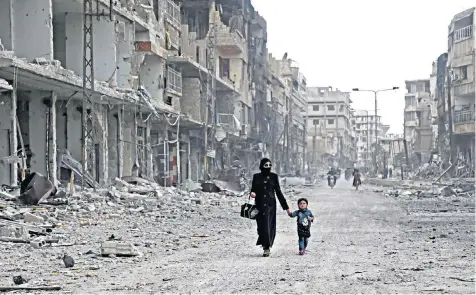  ??  ?? A Syrian woman and child walk down a destroyed street as civilians and rebels prepare to evacuate one of the few remaining rebel-held pockets in Arbin, Eastern Ghouta