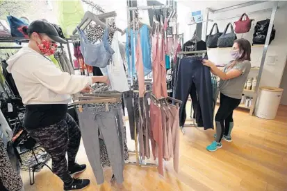  ?? JOHN MCCALL/SOUTH FLORIDA SUN SENTINEL ?? General manager Krystal Campi, left, and yoga instructor Luisa Jaramillo wear masks and stay 6 feet apart as they organize products at Fitness Hub Studios in West Palm Beach on Monday.