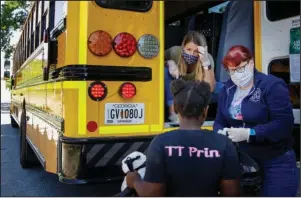  ?? The Associated Press ?? FEEDING SCHOOLCHIL­DREN: Teachers, Jennifer Scandle, left, and Renee Roberts, right, hand out a lunch to Kelsi Clarke, center, from a school bus as Chattahooc­hee County schools provide a last meal for their students before summer break on May 7 in Cusseta, Ga.