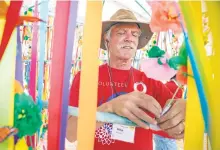  ?? GABRIELA CAMPOS/THE NEW MEXICAN ?? LEFT: Mike Mcgeary, in his fifth year of volunteeri­ng, helps secure ribbons Thursday on an art piece that will hang in the center of the Innovation Tent for the Internatio­nal Folk Art Market.