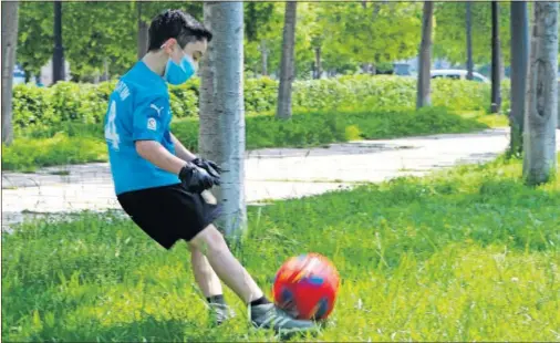  ??  ?? Imagen de estos días de un niño jugando al fútbol en un parque, protegido con unos guantes y una mascarilla.