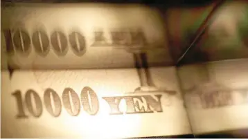  ?? — Reuters ?? Light is cast on a Japanese 10,000 yen note as it’s reflected in a plastic board in Tokyo.