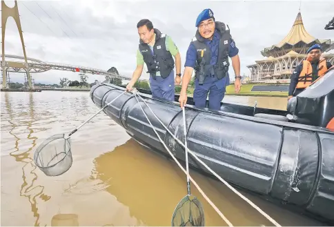  ?? — Photo by Kong Jun Lung ?? Zulkifli (left) together with Sallehudin fishing out rubbish from their speedboat at the Kuching Waterfront yesterday.