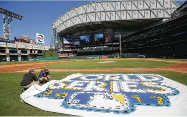  ?? Melissa Phillip / Houston Chronicle ?? Jake Cooley, left, and James Vaughn position a stencil for the World Series logo as the Astros ground crews ready Minute Maid Park for Friday’s Game 3.