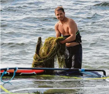  ??  ?? Markus Schmid vom SportCente­r am Mandichose­e zeigt, wie viel Unkraut dort wächst. Schon nach wenigen hundert Metern muss er wieder aufhören zu surfen, weil die Algen zu sehr bremsen.