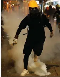  ?? AP/VINCENT THIAN ?? A protester prepares to throw back a tear-gas canister fired Saturday by officers near the police station in Hong Kong’s Tsim Sha Tsui district.