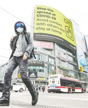  ?? PETER J. THOMPSON / FINANCIAL POST FILES ?? A pedestrian wearing a mask walks across Yonge Street at Dundas Street in downtown Toronto with a “Stop The Spread Of Covid 19” notice
in the background during the Covid 19 pandemic.