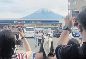  ?? THE ASSOCIATED PRESS ?? Visitors take a photo in front of a convenienc­e store at Fujikawagu­chiko, Japan, with a backdrop of
Mt. Fuji on Monday. The town began to set up a huge black screen on a stretch of sidewalk to block the view of the mountain.