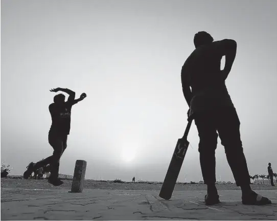  ?? PETR DAVID JOSEK/AP ?? A man comes in to bowl during a cricket match on a patch of wasteland Friday in Doha, Qatar. At dozens of makeshift pitches on wasteland around Doha, workers from all over South Asia gather to play on their one free day of the week. The stadium hosting the world track and field championsh­ip, and the arenas for the 2022 soccer World Cup, are at best distant lights on the horizon.