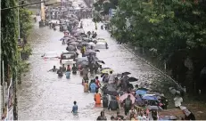  ?? FOTO: DPA ?? Menschen bahnen sich ihren Weg durch eine überflutet­e Straße in Mumbai. In den Fluten versanken auch mehrere Autos.