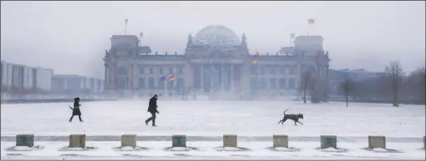  ?? (AP/Christoph Soeder) ?? Walkers with a dog cross in front of the German parliament, the Reichstag building, during snowfall in Berlin on Sunday.