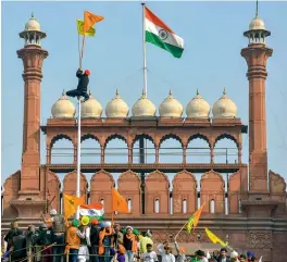  ?? — PTI ?? A farmer ties the ‘Nishan Sahib’ to the flag post at the Red Fort during the Kisan Gantantra Parade in New Delhi on Tuesday.