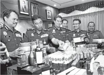  ??  ?? Hamidan (second, left) with other policemen showing the confiscate­d contraband items which consist of cigarettes, firecracke­rs and alcoholic drinks.