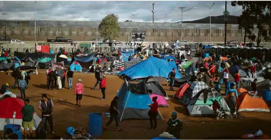  ?? Hannah McKay/Reuters ?? Acampament­o que abriga 3.000 imigrantes em campo de beisebol de Tijuana; ao fundo, o muro que divide o México e os EUA