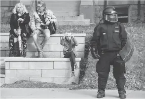  ?? PAUL CHIASSON / THE CANADIAN PRESS ?? A young girl takes a photo on her cellphone beside a police officer in riot gear as he stands watch ahead of a planned G7 protest in Quebec City on Thursday.