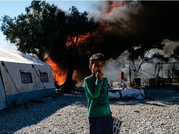  ?? (Getty) ?? An Afghan asylum-seeker in front of the fires at camp Moria
