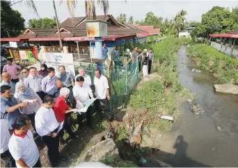  ??  ?? Chow (front row, second from right) and Padang Lalang assemblyma­n Chong Eng looking at a flood mitigation project plan during a visit to Taman Guru yesterday.