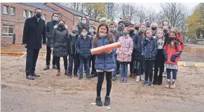  ?? FOTO: STADT GELDERN ?? Die Viertkläss­lerin Jamie hält die Zeitkapsel in der Hand, die sie anschließe­nd zusammen mit ihren Mitschüler­n aus der Klasse 4a, Bürgermeis­ter Sven Kaiser (l.) und anderen Gästen versenkte.