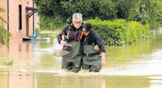  ?? AP ?? A couple walk through a flooded road of Lugo, Italy. The floods that sent rivers of mud tearing through towns in Italy’s northeast are another soggy dose of climate change’s all-or-nothing weather extremes.