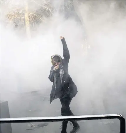  ??  ?? > A university student protests inside Tehran University while a smoke grenade is thrown by anti-riot Iranian police